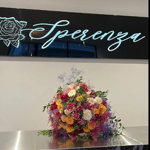 Photo de l'avis : le comptoir de la boutique sous l'enseigne lumineuse Sperenza, avec un grand bouquet coloré